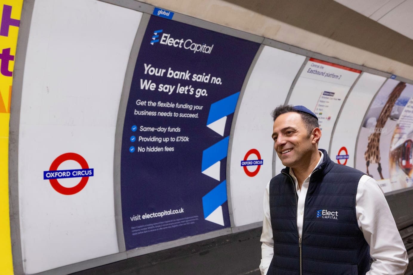 An Elect Capital team member beside an Elect Capital advert on the London Underground